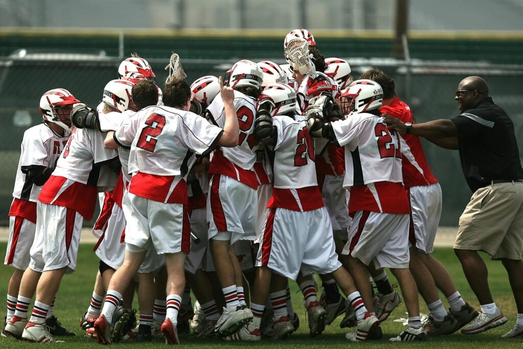 A group of lacrosse players and their coach celebrating a victory on the field.