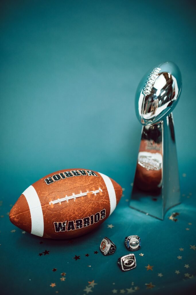 Football trophy and rings with a football on blue background, symbolizing victory and achievement.