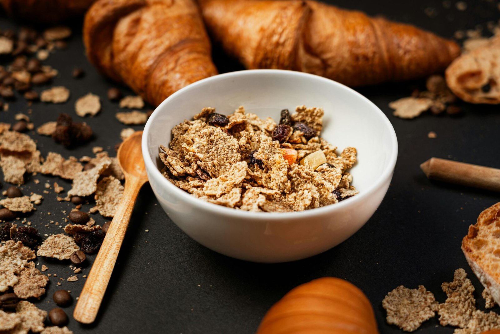 Fresh croissants with a bowl of cereal featuring raisins and nuts for a tasty breakfast.